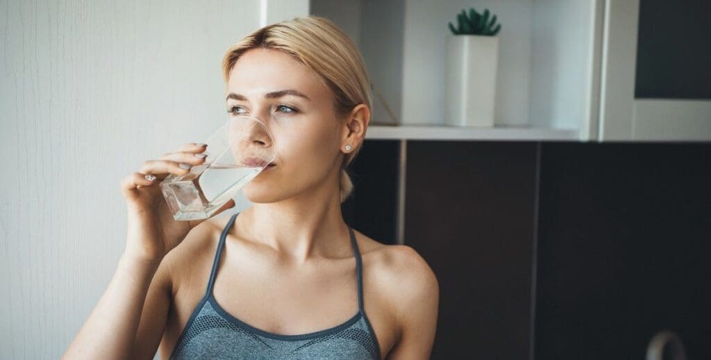 Young fitness lady drinking water after yoga exercises wearing sportswear at home dry mouth general dentistry dentist in Mount Pleasant Michigan